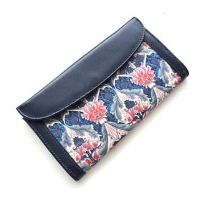 May include: A navy blue clutch wallet with a flap closure. The wallet features a floral pattern in shades of red, pink, blue, and white. The design is a mix of flowers and leaves. The wallet is made of leather and fabric.