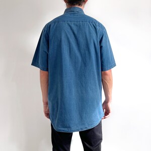 K&ouml;nnte beinhalten: Ein blaues, kurz&auml;rmeliges Hemd aus Denim mit Knopfleiste.