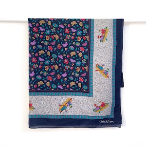 May include: A navy blue silk scarf with a floral print and a white border. The border features a repeating pattern of small boats with people in them. The scarf is signed "Cacharel de France".