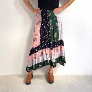 Puede incluir: Una falda larga y asimétrica con un diseño de patchwork que presenta patrones florales en rosa, verde, negro y blanco. La falda tiene un dobladillo con volantes y está hecha de una tela ligera.