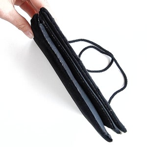May include: A black velvet evening bag with a black cord handle. The bag is folded in half and the handle is looped around the bag.