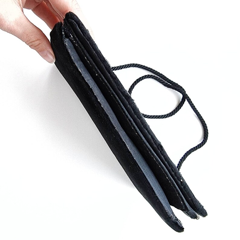 May include: A black velvet evening bag with a black cord handle. The bag is folded in half and the handle is looped around the bag.