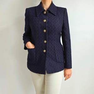 Op de afbeelding: Een marineblauwe blazer met een textuurpatroon, een reverskraag en goudkleurige knopen. De blazer heeft twee voorzakken en wordt gedragen met een crèmekleurige broek. De jas is een klassieke stijl.