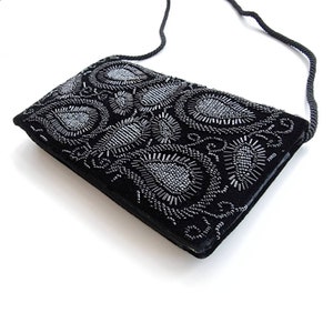 May include: A black velvet evening bag with a silver beaded paisley design. The bag has a long black strap.