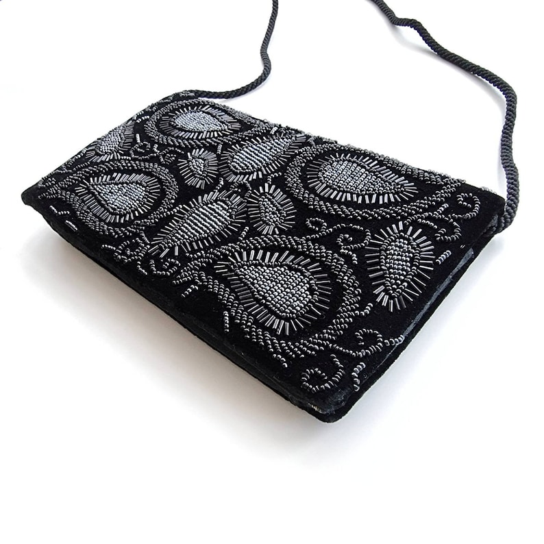 May include: A black velvet evening bag with a silver beaded paisley design. The bag has a long black strap.