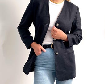 May include: A black linen blazer with a single button closure and a v-neck. The blazer is worn over a white t-shirt and blue jeans.