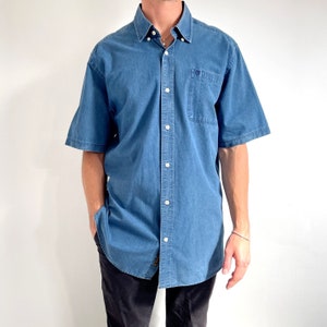 K&ouml;nnte beinhalten: Ein blaues, kurz&auml;rmeliges Hemd aus Denim mit einer Brusttasche.