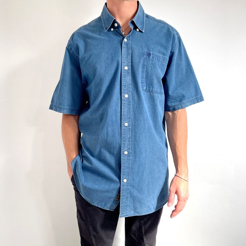 K&ouml;nnte beinhalten: Ein blaues, kurz&auml;rmeliges Hemd aus Denim mit einer Brusttasche.