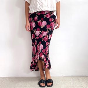 May include: A black floral skirt with a pink and red rose pattern. The skirt has a ruffled hem and is knee-length. The skirt is made of a lightweight fabric.
