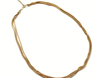 May include: A gold-toned necklace with a multi-strand design. The necklace features three delicate strands that are intertwined and connected with an adjustable chain and clasp. The jewelry is set against a white background.