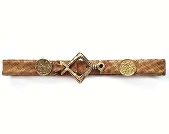 May include: A tan leather belt with a textured pattern. The belt features a diamond-shaped buckle and two circular decorative elements. The buckle and decorative elements have a gold finish. The belt is approximately 1.5 inches wide.