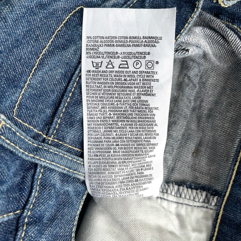 May include: A white care label with black text detailing washing instructions for a garment. The label includes a 30 degree Celsius washing symbol, a triangle with an X inside, a square with a circle inside, a circle with a P inside, and a circle with a circle inside. The text includes the following: "70% Cotton-Katoen-Coton-Bomull-Baumwolle-Cotone-Algod&oacute;n-Bomuld-Puuvilla-Algod&atilde;o-Bamabaki-Pamuk-Bawełna-Pamut-Bavlna-Bombaž 30% Lyocell/Tencel&reg; - &Lambda;&Upsilon;&Omicron;&Sigma;&Epsilon;&Lambda;/TENCEL&reg; - Liocelna Vl/Tencel-Liocel/Tencel&reg;"
