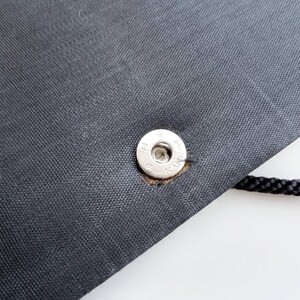 May include: Close-up of a black fabric bag with a silver snap closure. The snap has the text "K-SNAP" printed on it.