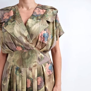May include: A vintage wrap dress with a floral print in shades of green, brown, blue, and pink. The dress has a V-neckline, short sleeves, and a pleated skirt.