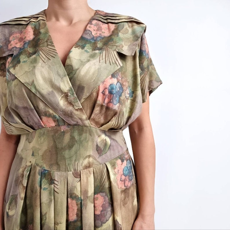 May include: A vintage wrap dress with a floral print in shades of green, brown, blue, and pink. The dress has a V-neckline, short sleeves, and a pleated skirt.