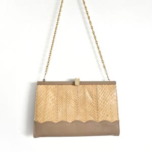May include: A beige snakeskin clutch with a gold chain strap and a brown leather bottom. The clutch has a scalloped edge and a gold clasp.