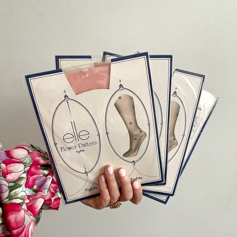 May include: A stack of four pink and white patterned tights with the brand name "elle Flower Pattern tights" printed on the front. The tights feature a floral design and are packaged in clear plastic.