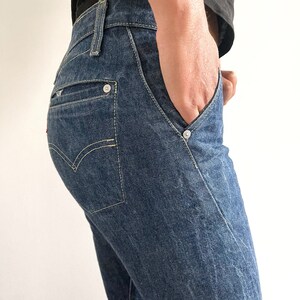 May include: Close-up of a pair of blue denim jeans with a single button on the back pocket.