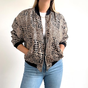 May include: A brown and black snake print bomber jacket with a black zipper and black ribbed trim.