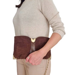 May include: A brown suede clutch bag with a gold chain strap and a gold clasp. The bag has a snakeskin panel on the front.