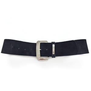 Op de afbeelding: Een brede zwarte riem met een grote, vierkante zilverkleurige gesp. De riem is gemaakt van een suède-achtig materiaal en heeft een bijpassende zilverkleurige riemlus. De riem is ontworpen om om de taille te worden gedragen.