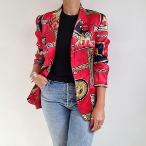 Puede incluir: Una chaqueta de satén roja con un diseño estampado en dorado y negro. El patrón presenta formas geométricas y figuras estilizadas.