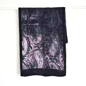 May include: A dark scarf featuring a paisley pattern in shades of purple, silver, and black. The scarf has a black velvet border and is displayed against a white backdrop. The paisley design is detailed and intricate.