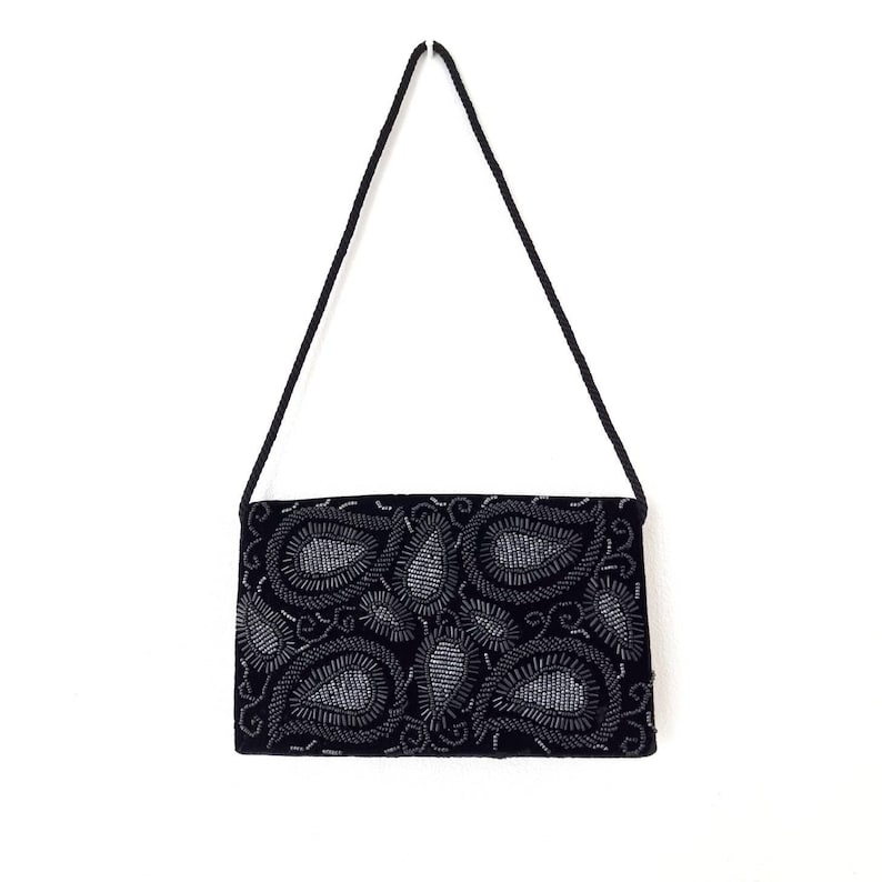 May include: A black velvet evening bag with a silver paisley design. The bag has a long strap.