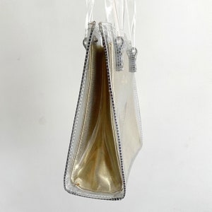 May include: A clear plastic tote bag with a gold lining and two silver zipper pulls.