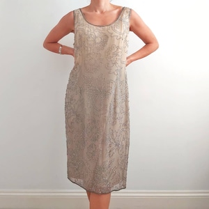Puede incluir: Un vestido beige sin mangas con un estampado floral hecho de cuentas plateadas.