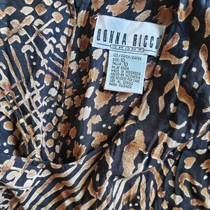 May include: A black and brown rayon dress with a leopard print pattern. The dress has a tag that reads "Donna Ricco Sport" and includes the size 10, the fabric content, and the country of origin.