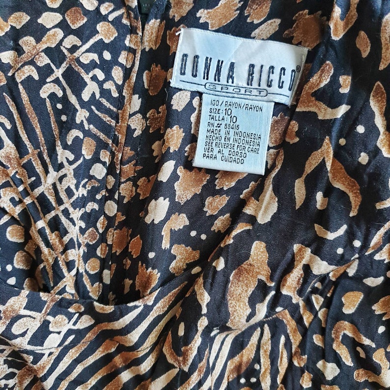 May include: A black and brown rayon dress with a leopard print pattern. The dress has a tag that reads "Donna Ricco Sport" and includes the size 10, the fabric content, and the country of origin.