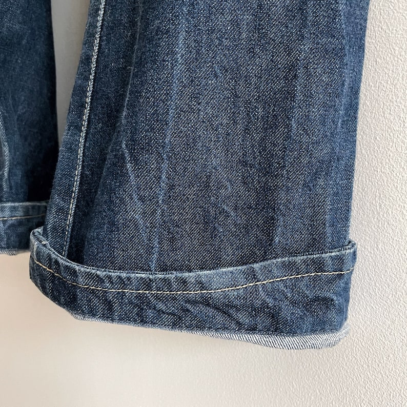 May include: Close-up of the hem of a pair of blue denim jeans with a single stitch of light yellow thread running along the edge.
