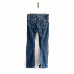May include: A pair of dark blue denim jeans with cuffed hems hanging on a hanger against a white background.