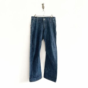 May include: A pair of dark blue denim jeans hanging on a hanger against a white background.