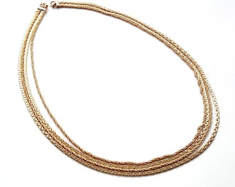 May include: A gold layered chain necklace with multiple strands of different widths. The necklace is made of a delicate, interwoven chain pattern.