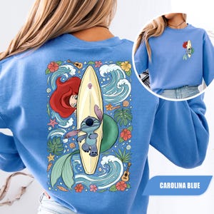 May include: A Carolina blue sweatshirt featuring a large back graphic of Ariel and Stitch with a surfboard, surrounded by tropical flowers, waves, and ukuleles. A smaller version of the same graphic is printed on the front left chest area.
