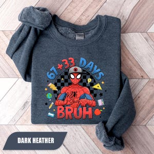 May include: Dark heather gray sweatshirt featuring a graphic of Spider-Man with the text "67+33 DAYS BRUH". The design includes school-themed elements like pencils, stars, and a globe. The words "DARK HEATHER" are at the bottom.