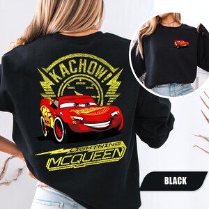 May include: A black sweatshirt featuring a large graphic on the back of a red race car with the text KACHOW and LIGHTNING MCQUEEN in yellow. A smaller version of the same red race car is printed on the front left chest area of the garment.