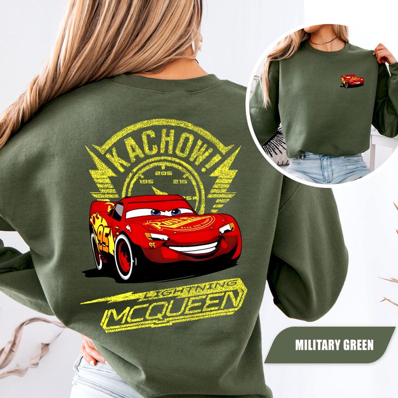 May include: An olive green crewneck sweatshirt featuring a large graphic on the back of the red race car Lightning McQueen with the text KACHOW and LIGHTNING MCQUEEN in yellow. A smaller version of the car is printed on the front left chest area.