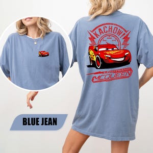 May include: A blue jean colored t-shirt featuring a small Lightning McQueen graphic on the front left chest and a large graphic on the back displaying Lightning McQueen, a speedometer, the text KACHOW!, and the name LIGHTNING MCQUEEN.