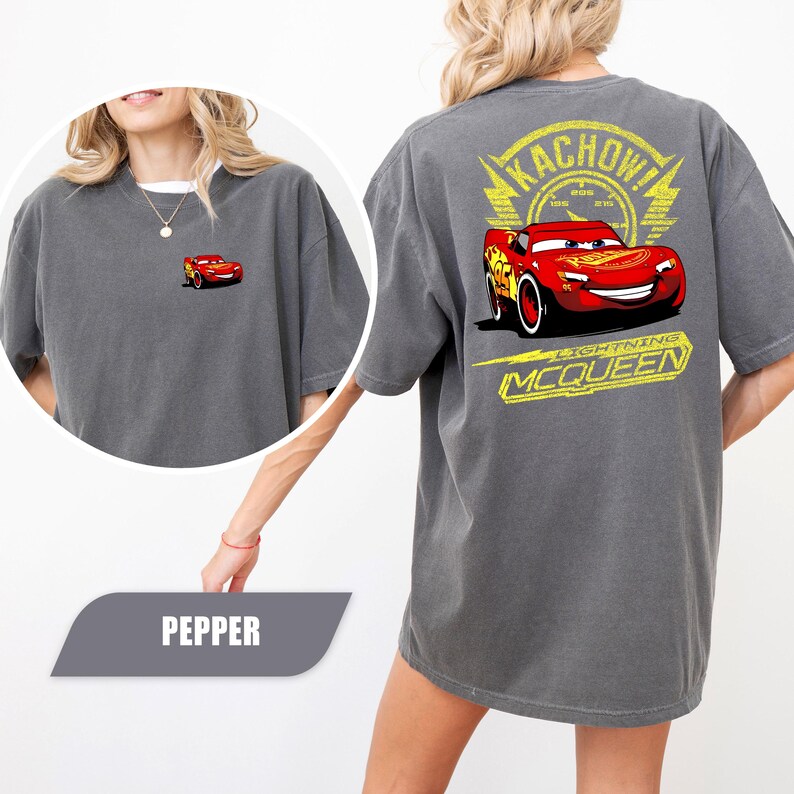 May include: A charcoal gray t-shirt featuring a small graphic of the red race car Lightning McQueen on the front left chest. The back displays a large graphic of Lightning McQueen with the text KACHOW! and LIGHTNING MCQUEEN in yellow.