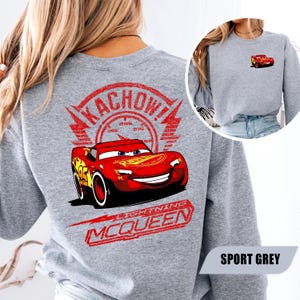 May include: A sport grey sweatshirt featuring a large graphic on the back of the red race car Lightning McQueen with the text KACHOW! and LIGHTNING MCQUEEN. A smaller version of the same red race car graphic is printed on the front left chest area.