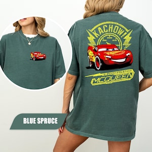 May include: A blue spruce t-shirt featuring a small graphic of Lightning McQueen on the front left chest and a large graphic on the back with the text KACHOW! and LIGHTNING MCQUEEN surrounding the red race car character with the number 95.