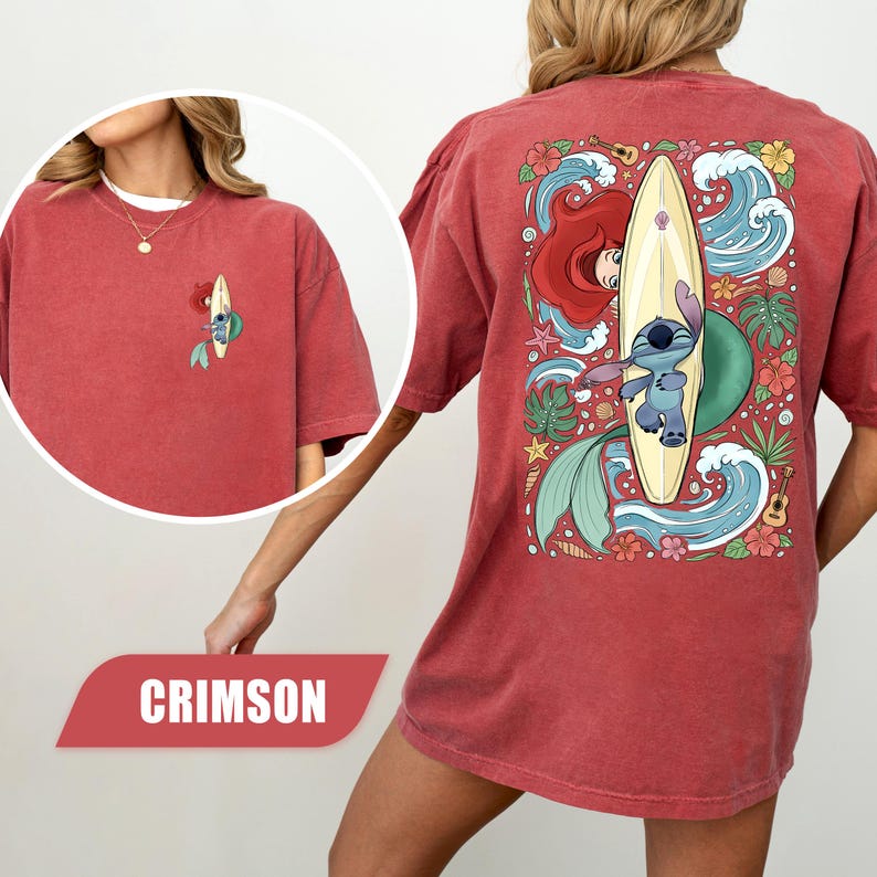 May include: A crimson short-sleeve t-shirt featuring a small graphic on the front left chest and a large graphic on the back. The back design displays a blue alien character on a surfboard, a red-haired mermaid, ocean waves, and tropical flowers.