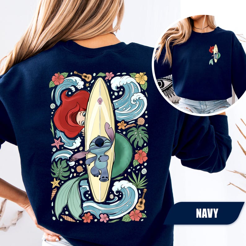 May include: A navy blue crewneck sweatshirt featuring a large graphic on the back and a smaller version on the front left chest. The design depicts a cartoon character with a surfboard, a mermaid, tropical flowers, waves, and a small guitar.