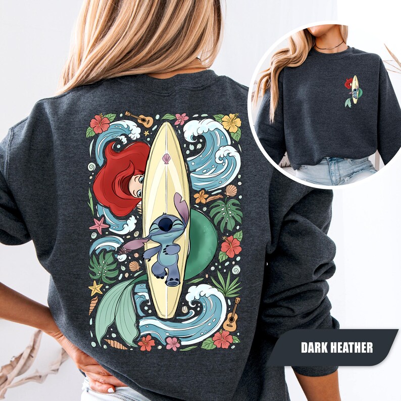 May include: A dark heather gray crewneck sweatshirt featuring a large back graphic of a blue alien character on a surfboard, a red-haired mermaid, tropical flowers, green leaves, ocean waves, and a small guitar. A small matching graphic is on the front.