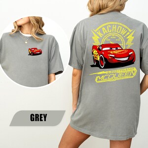 May include: A grey t-shirt featuring a small graphic of the red race car Lightning McQueen on the front left chest. The back displays a large graphic of Lightning McQueen with the text KACHOW! and LIGHTNING MCQUEEN in yellow.