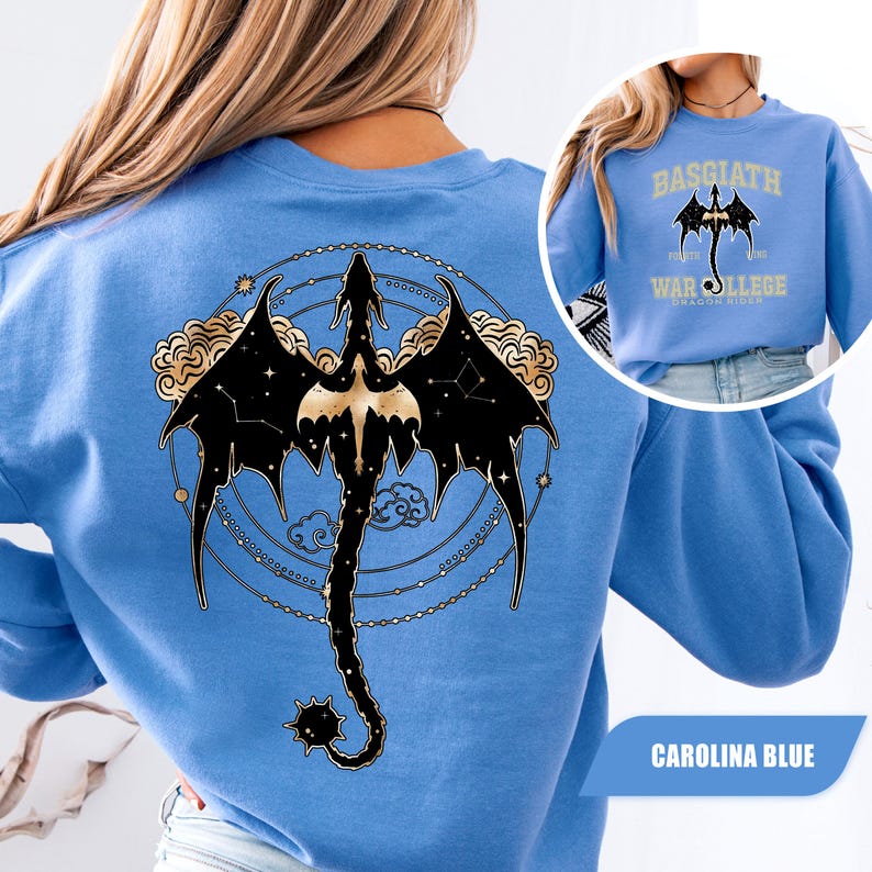 May include: Carolina blue sweatshirt featuring a black dragon design with gold accents on the back. The dragon is surrounded by a constellation and cloud design. The front of the sweatshirt has a smaller image of the dragon and the text "BASGIATH WAR COLLEGE DRAGON RIDERS".