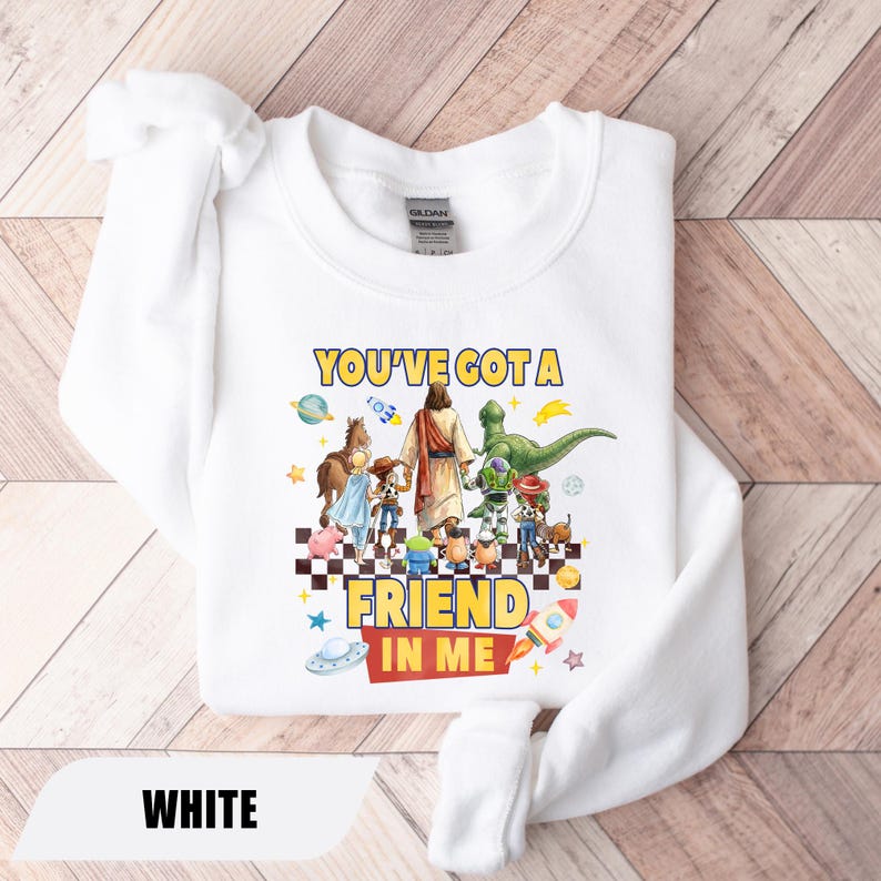 May include: A white long-sleeve sweatshirt featuring a graphic print of a central figure holding hands with various animated characters. The text "YOU'VE GOT A FRIEND IN ME" is printed in yellow and red. The design includes planets, stars, and a rocket.